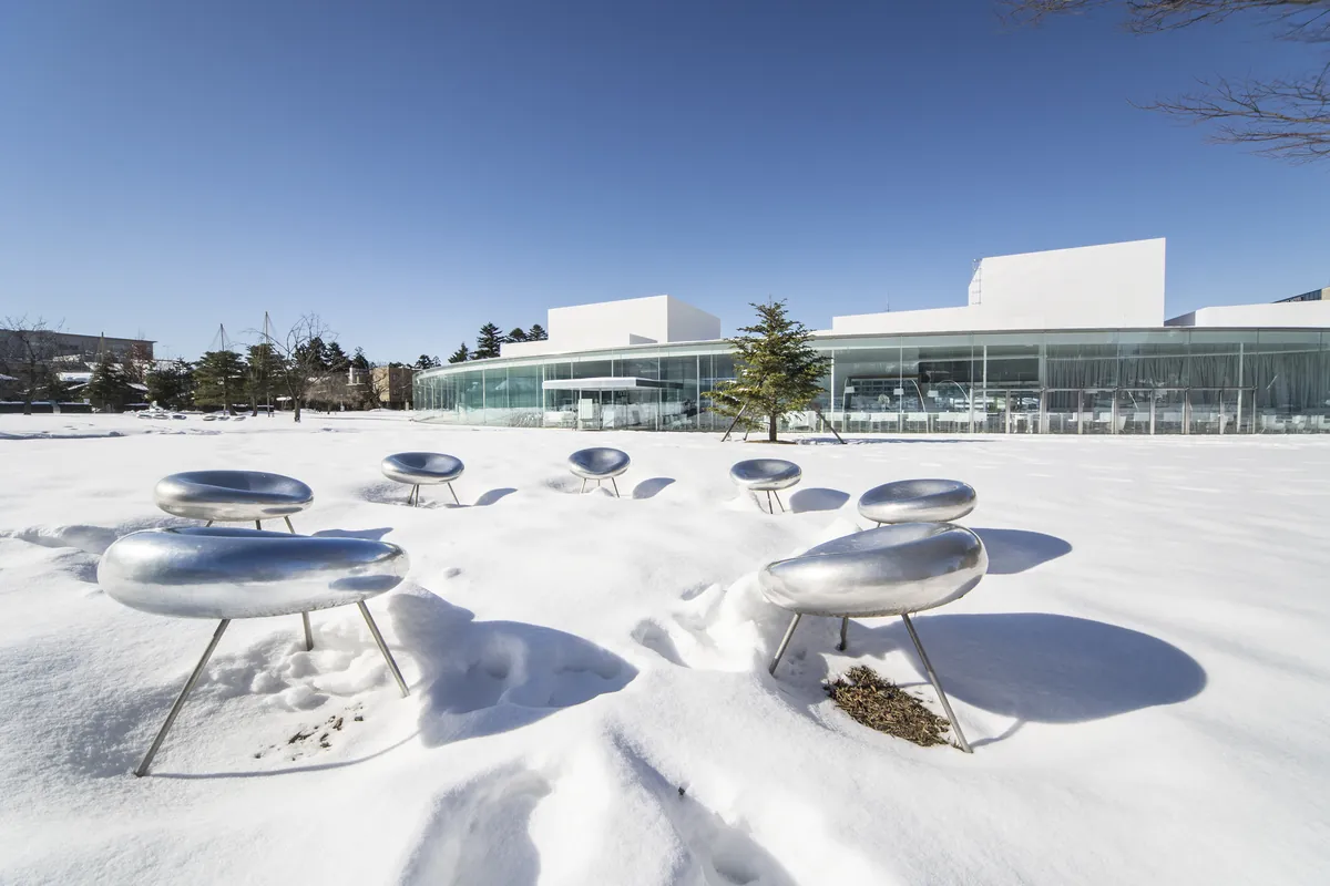 SANAA-designed circular glass facade of the 21st Century Museum of Contemporary Art with silver chair installation in winter snow