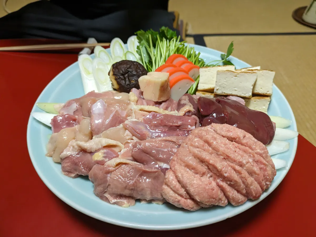 A platter of raw chicken pieces, tofu, mushrooms, and vegetables prepared for a Nagoya Cochin chicken hot pot