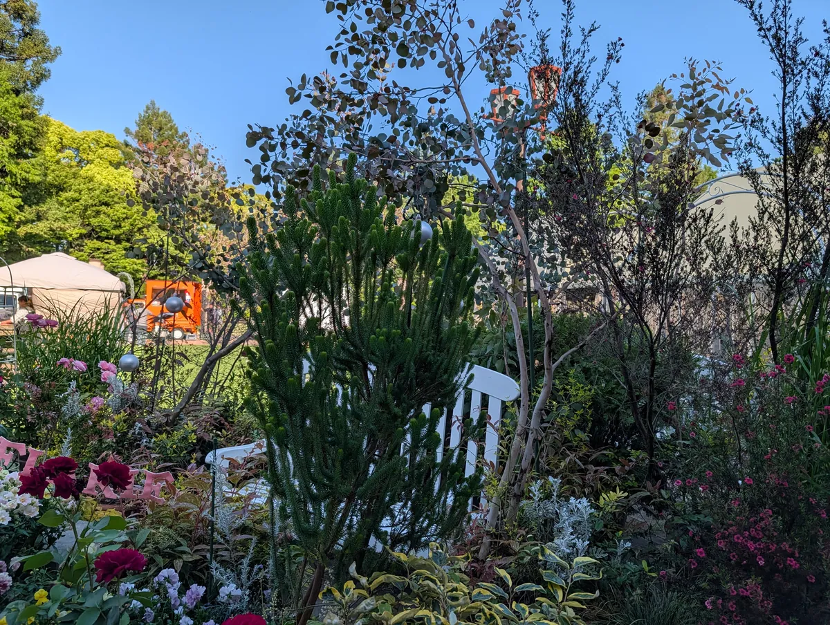 Mixed perennial border at Flarie with sculptural ornaments and a white garden chair tucked among flowering shrubs