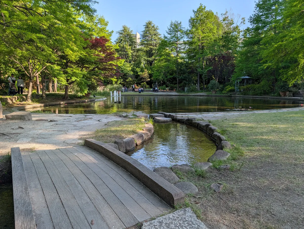 A small wooden bridge over a stone-lined inlet at Flarie's pond, with a lawn area visible beyond