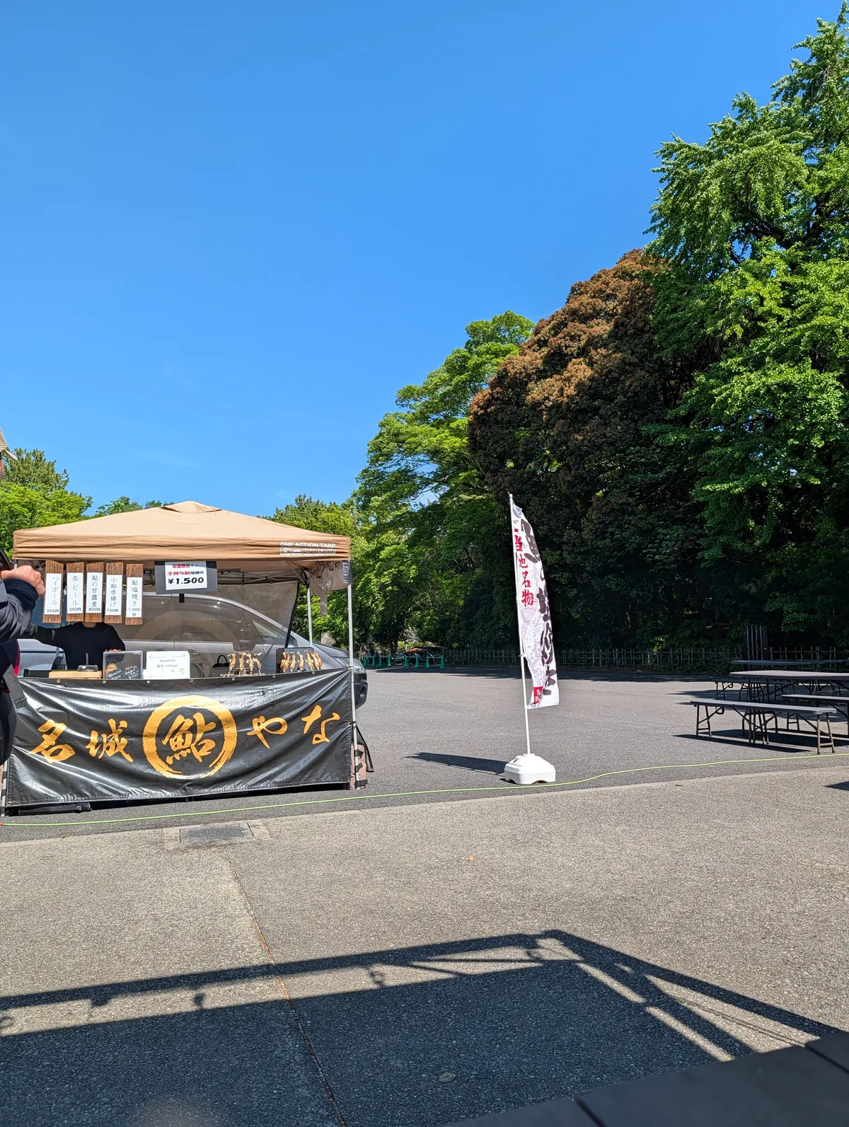 A pop-up Meijo Ayuyana grilled-ayu fish stall set up in the open area of Kinshachi Yokocho, with a black tent and benches under a clear sky