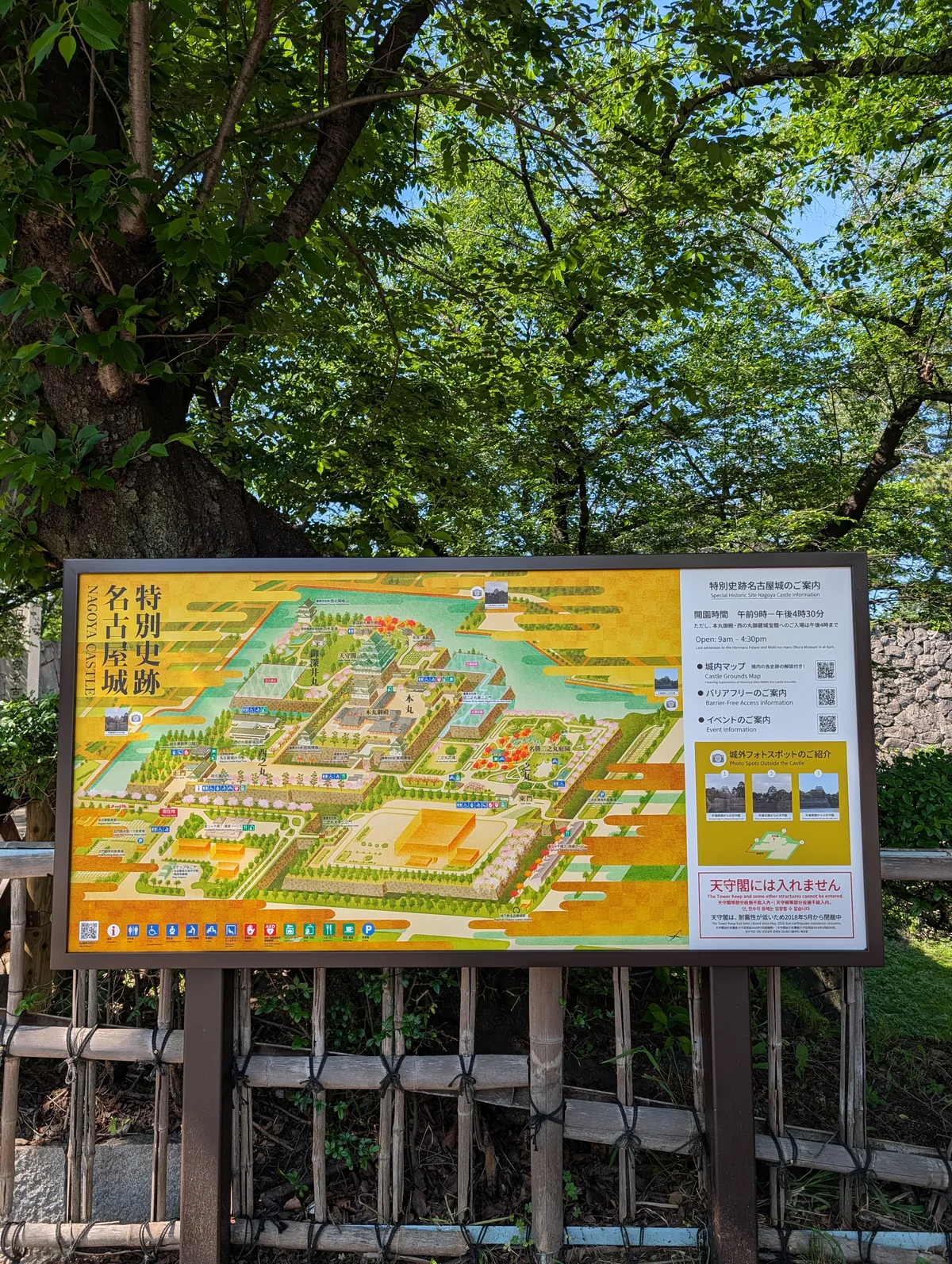 A large illustrated map of the Nagoya Castle special historic site grounds, mounted on a wooden frame and surrounded by spring greenery