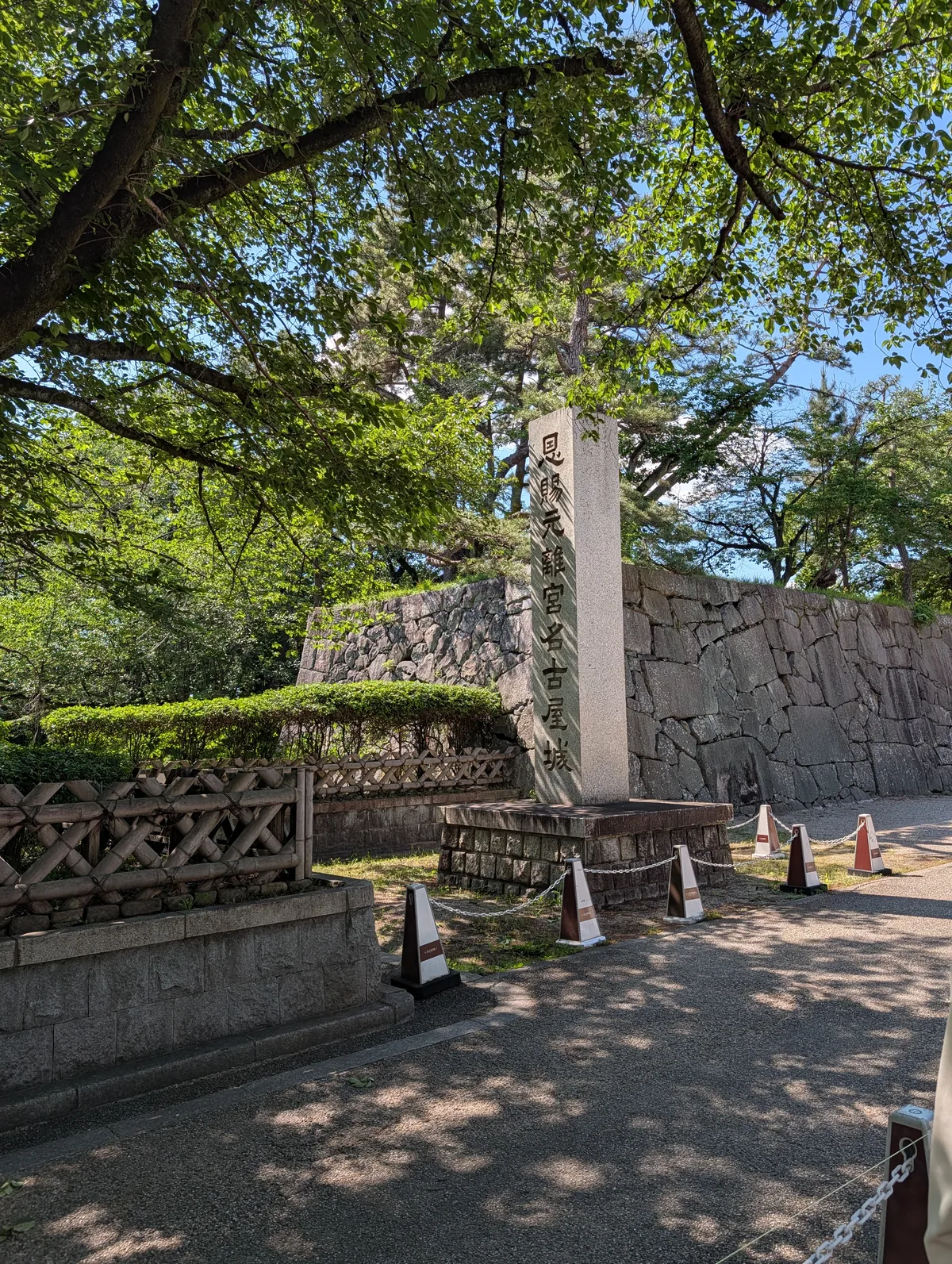 The 'Special Historic Site Nagoya Castle' stone monument standing beside the inner stone walls, framed by overhanging green branches