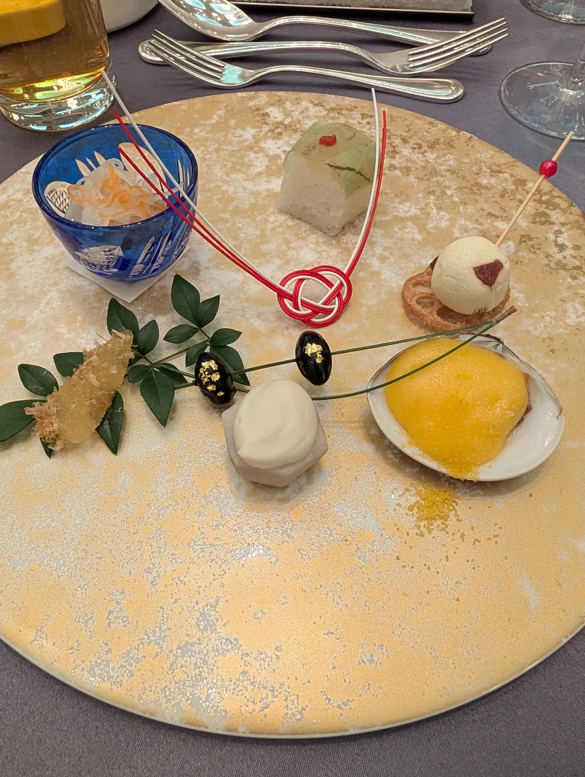 An artful Japanese-style dessert plate at the Marriott Associa with mochi, sorbet, candied citrus, and a red mizuhiki decorative cord on a gold-flecked round ceramic plate
