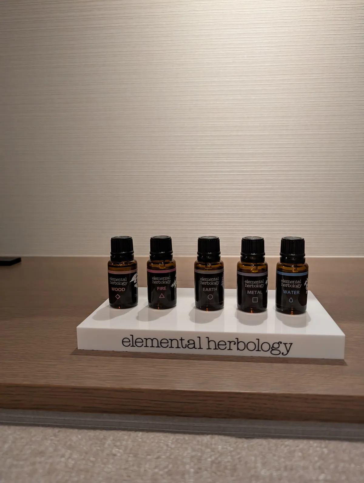 Five Elemental Herbology aromatherapy oil bottles labelled Wood, Fire, Earth, Metal, and Water on a display tray inside the TIAD spa