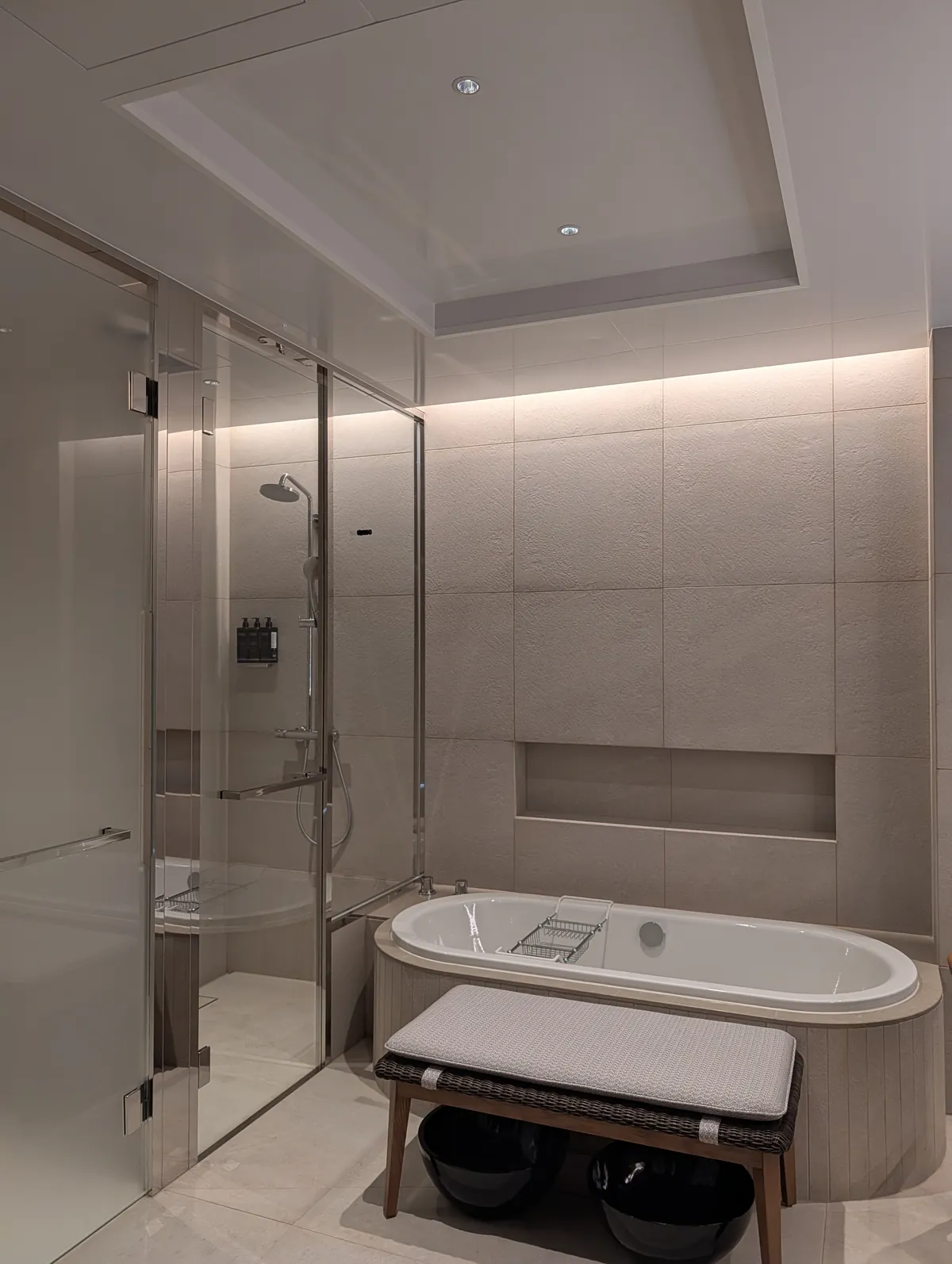 Spa bathroom inside TIAD with a glass shower booth, soaking tub, and beige tile finish