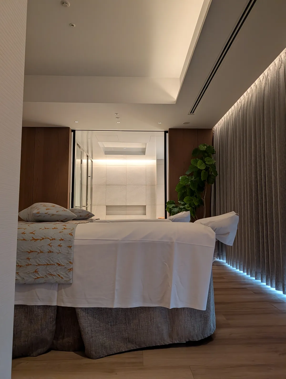 A twin-bed couple treatment room inside TIAD spa, lit indirectly with neutral wood tones and curtain detail