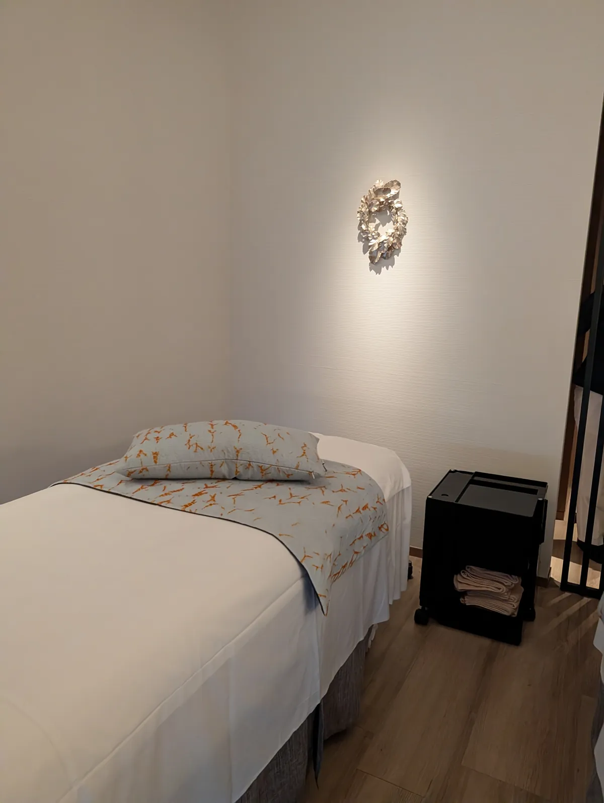 A serene single treatment bed inside the TIAD spa with a backlit decorative wall sconce