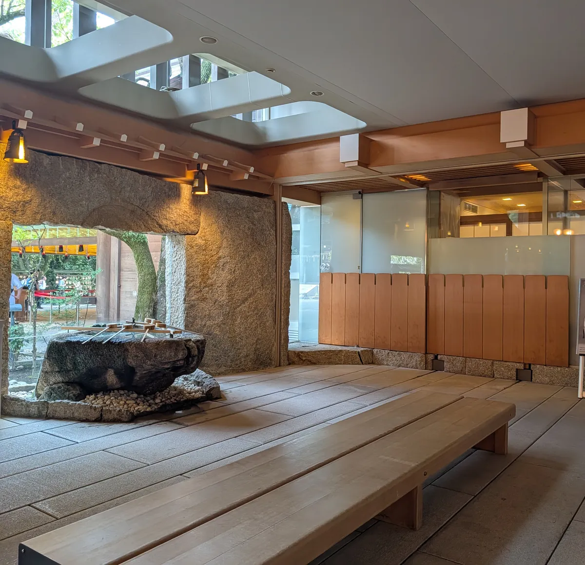 Sheltered purification pavilion at Atsuta Jingu: a huge rough stone basin with three bamboo dippers set against a cut-rock wall, with a low wooden bench alongside
