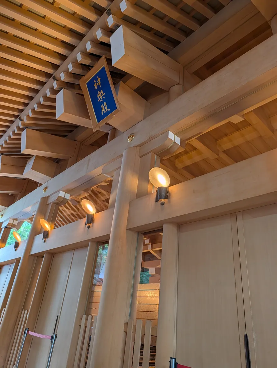 Blue lacquered plaque with gold calligraphy reading Kagura-den, hung under the pale cypress bracket work of a hall at Atsuta Jingu
