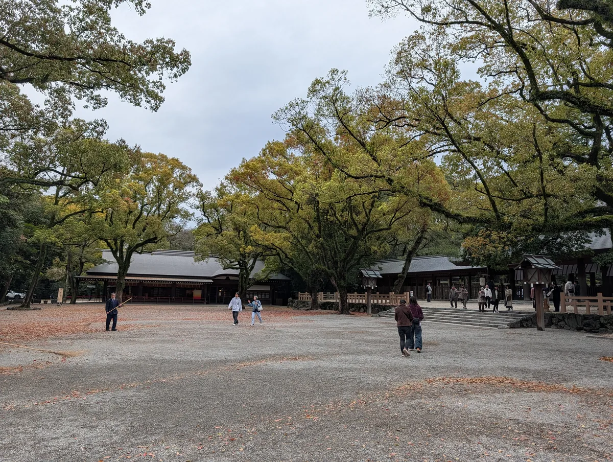 The wide gravel courtyard of Atsuta Shrine in Nagoya, framed by large camphor trees with shrine buildings behind