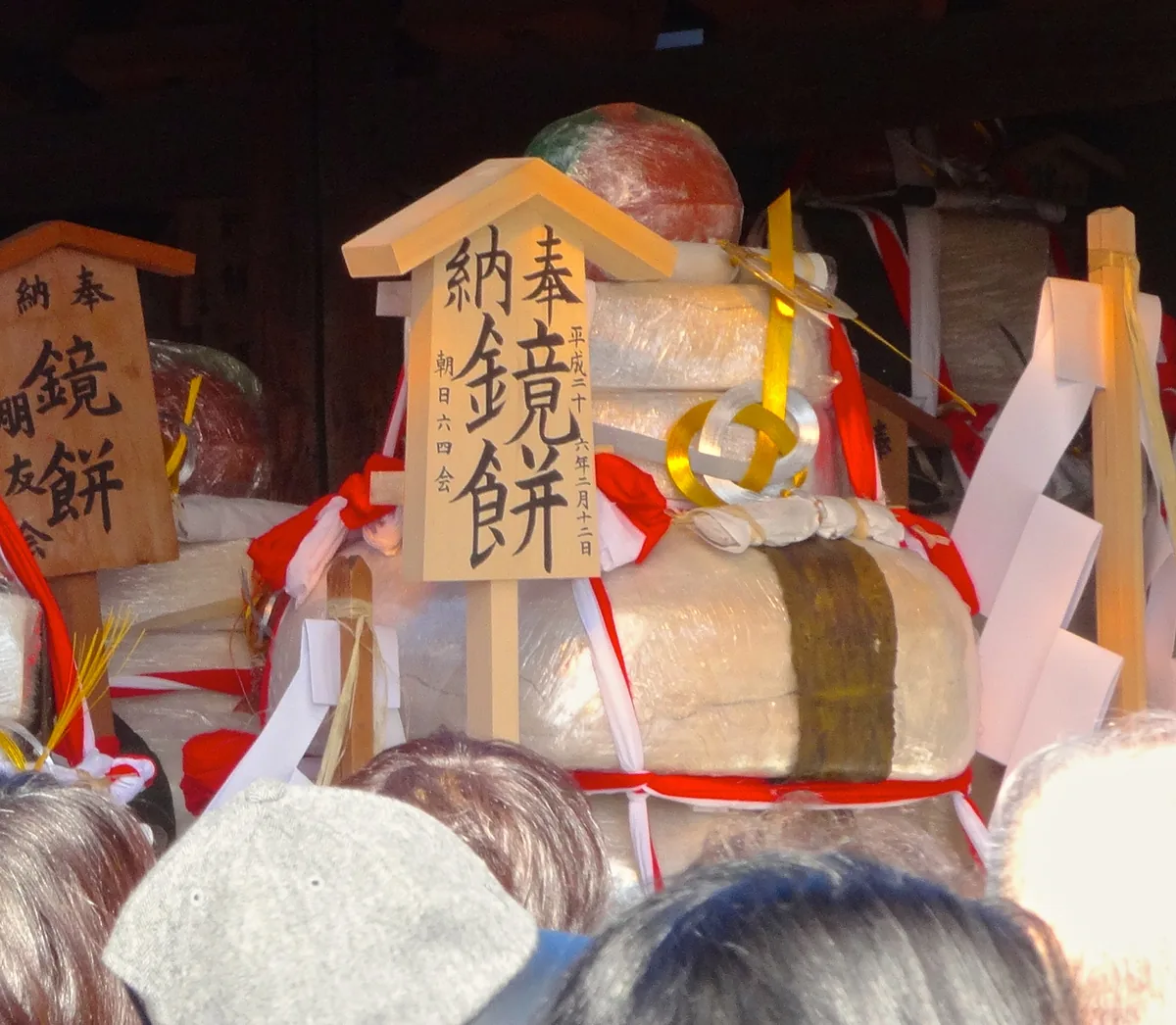 A giant stacked kagami-mochi rice cake offering with wooden votive tablets, seen over spectators