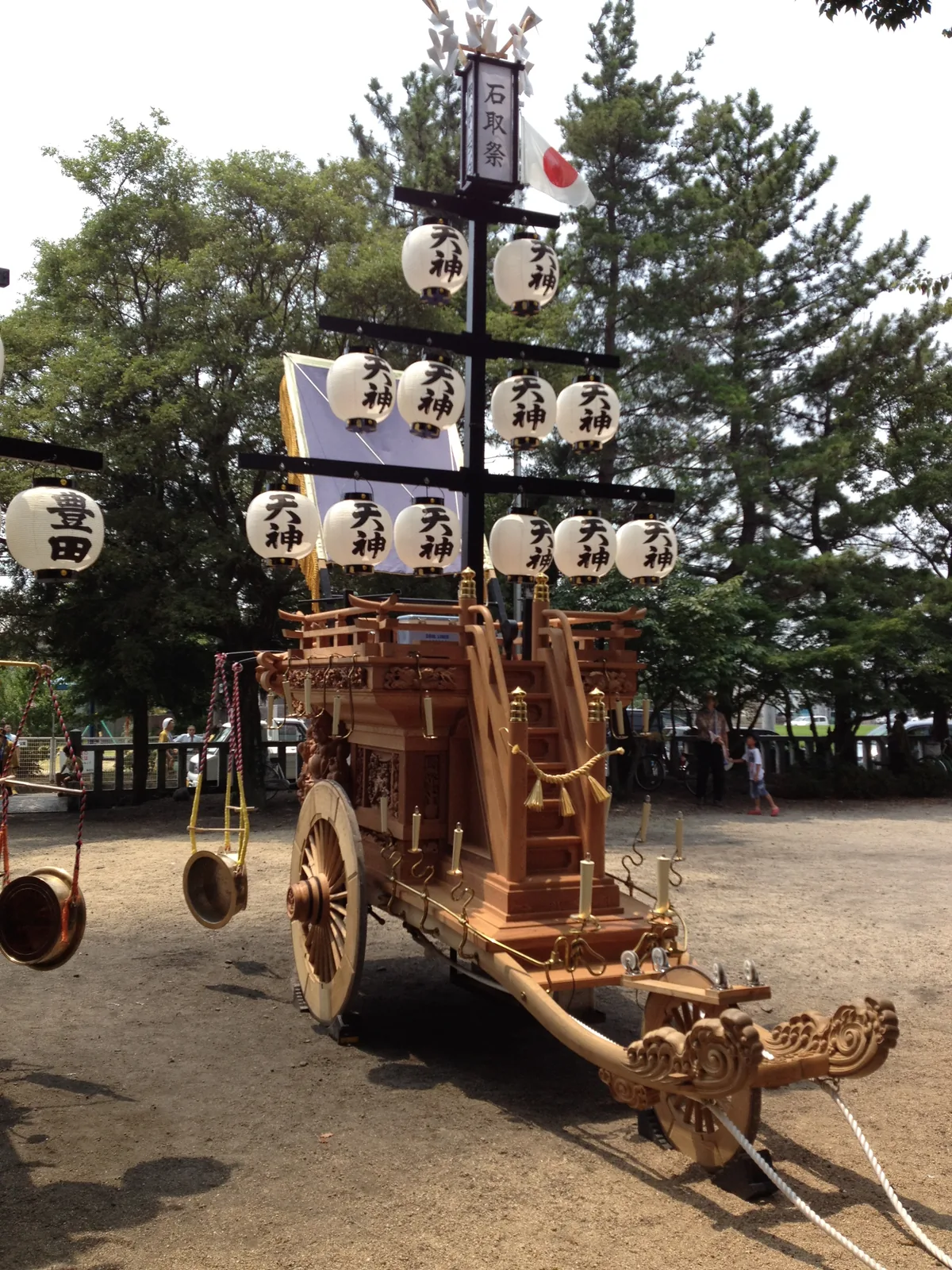 A wooden Ishidori festival cart hung with white paper lanterns, with bronze gongs hanging in front