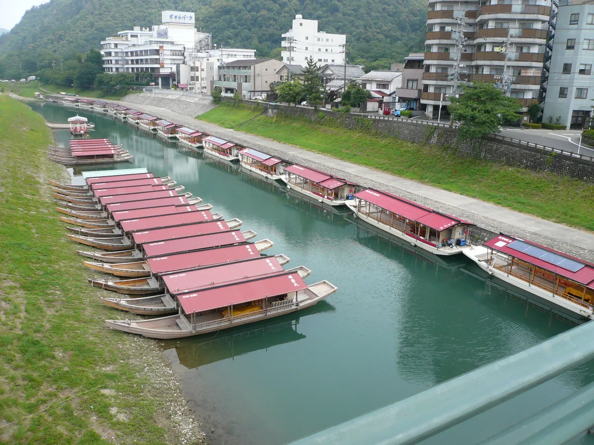 Wooden boats with red awnings moored side by side along the Nagara River below riverside buildings