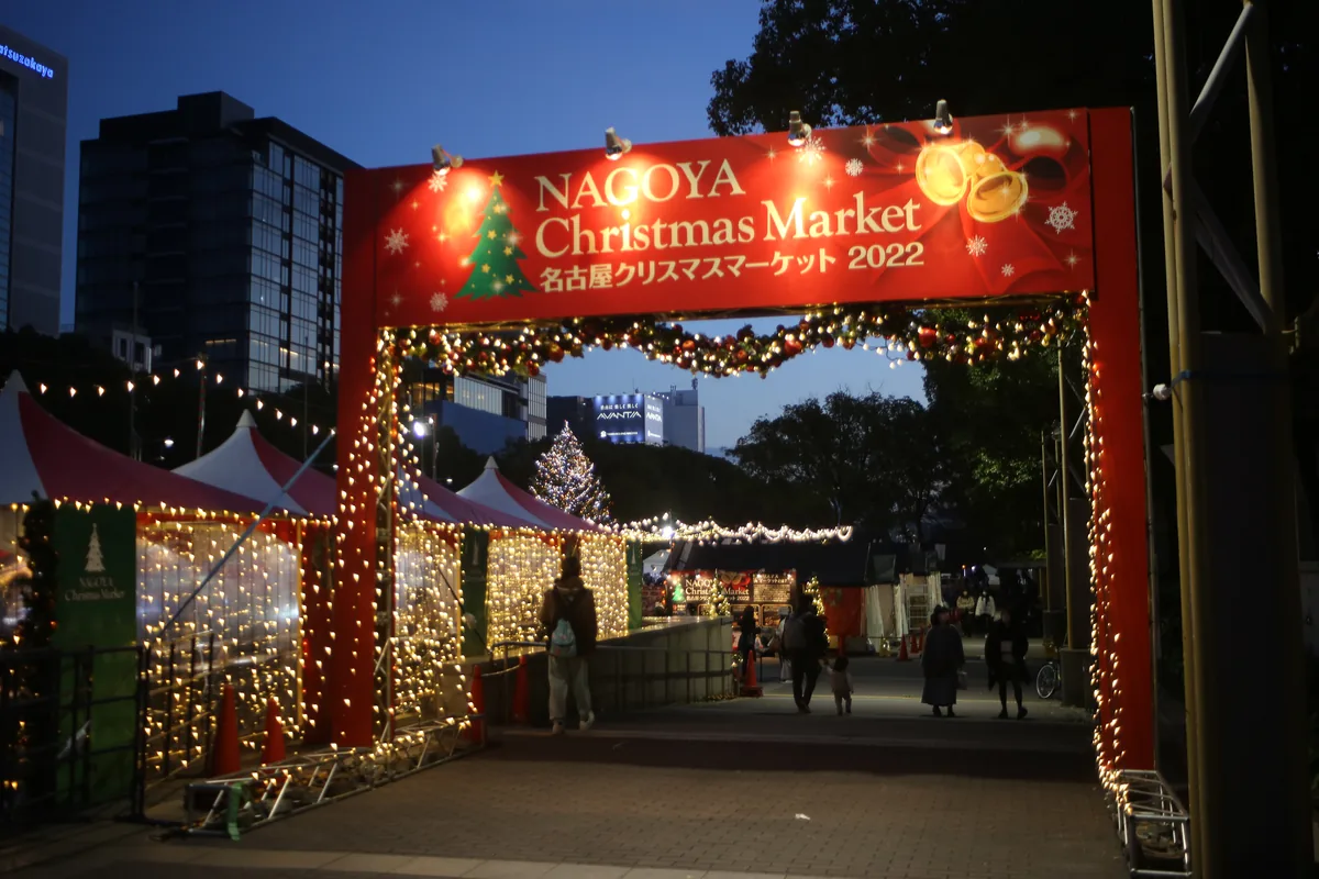 A red illuminated entrance arch for the Nagoya Christmas Market, with lit white stall tents behind