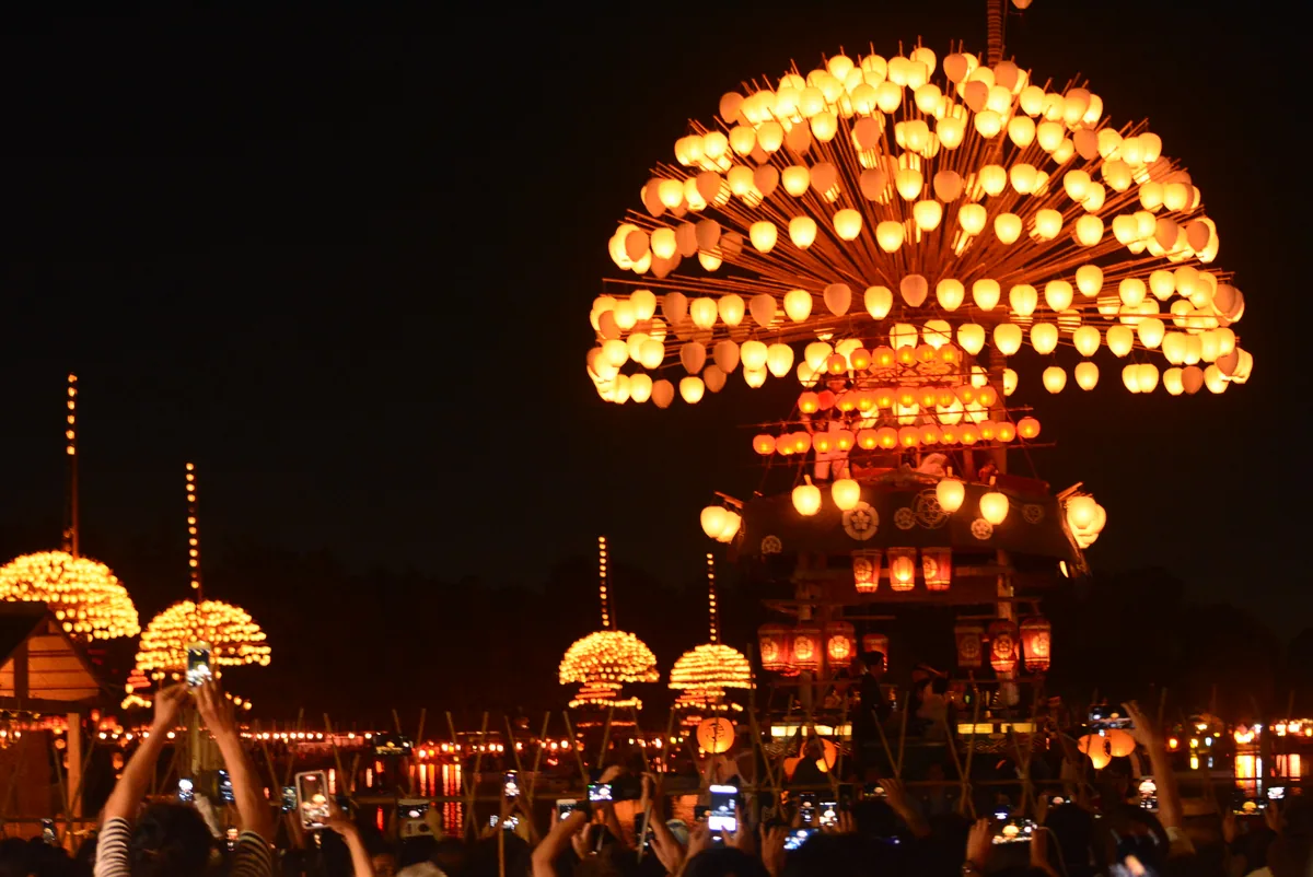 A boat hung with hundreds of glowing paper lanterns in a semicircle floats on a river at night