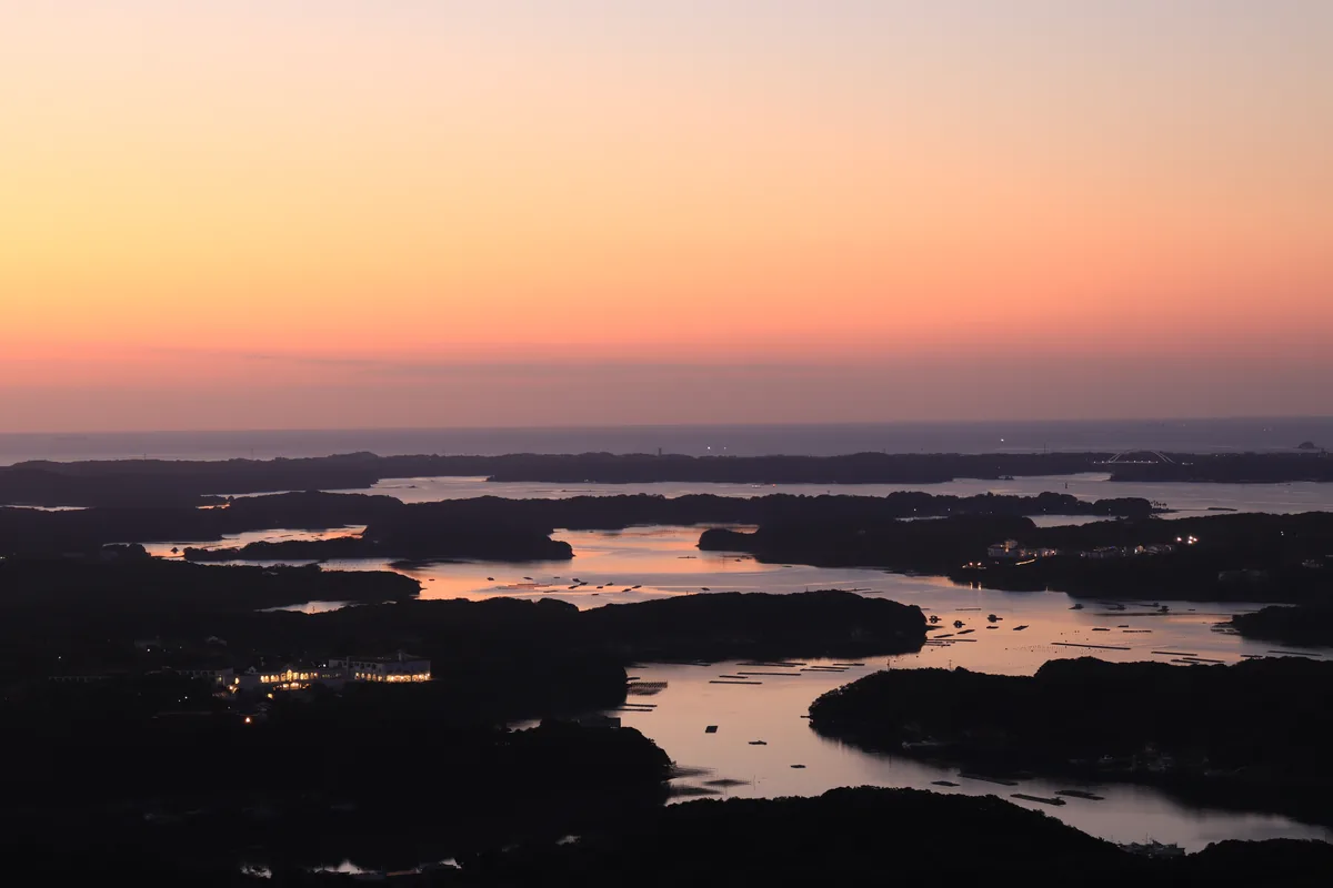 Dusk over a deeply indented bay with wooded islands, aquaculture rafts and scattered village lights