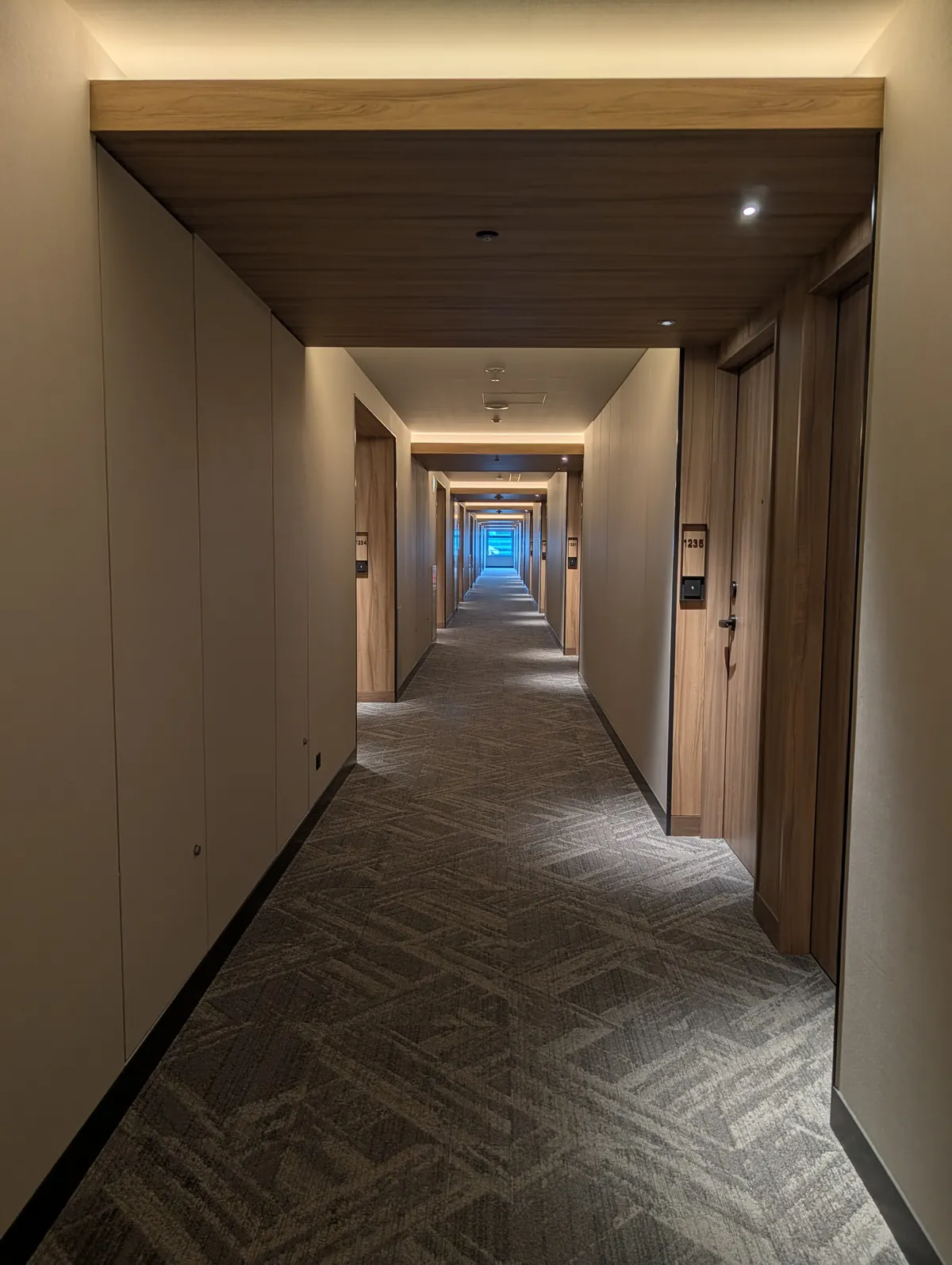 A long twelfth-floor guest corridor at Courtyard by Marriott Nagoya, with a slatted wooden ceiling and warm indirect lighting running its length