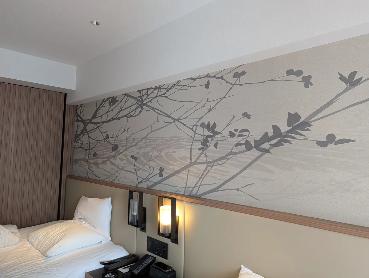 Close view of the guest room wall artwork at Courtyard by Marriott Nagoya, showing painted branches and leaves in earth tones inspired by the Horikawa river
