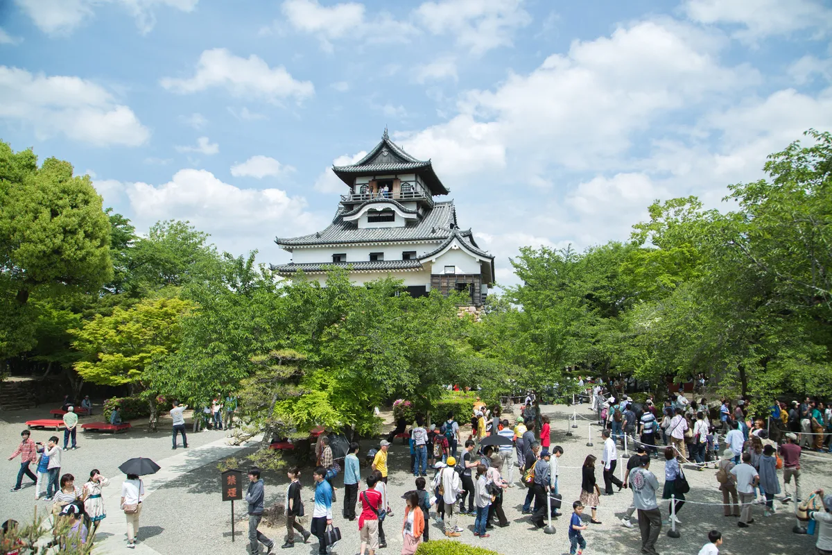 The wooden keep of Inuyama Castle seen from the courtyard below, with visitors gathered on the approach in front of it.