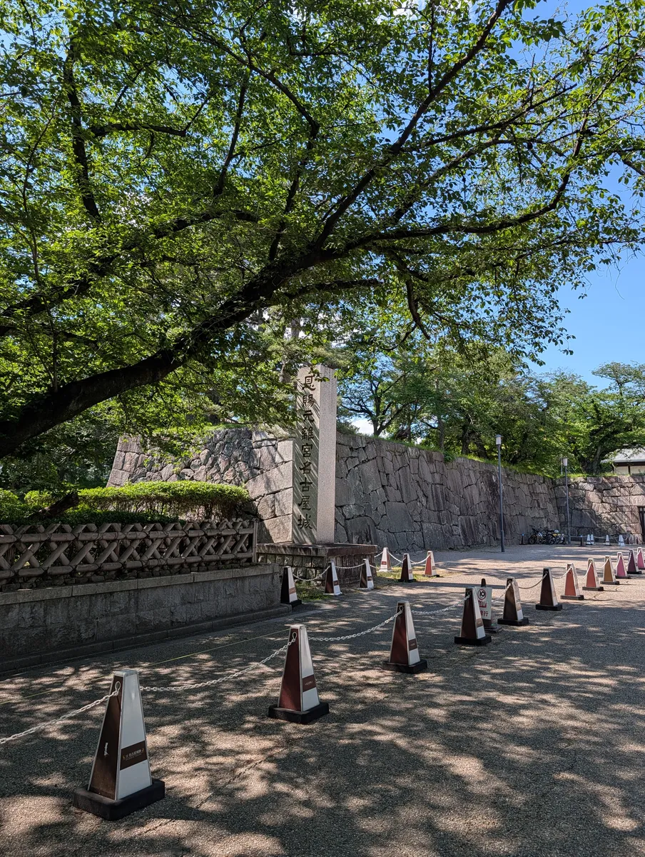 A tall inscribed stone monument standing in front of the massive fitted stone wall that rings the Nagoya Castle grounds.
