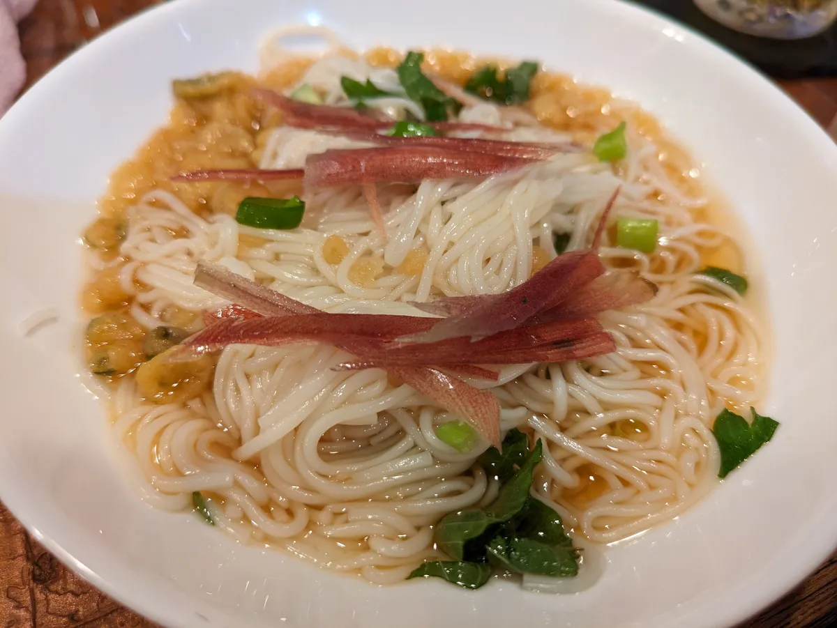 A bowl of thin white somen noodles in a light dashi broth topped with shredded myoga, spring onion and mitsuba.