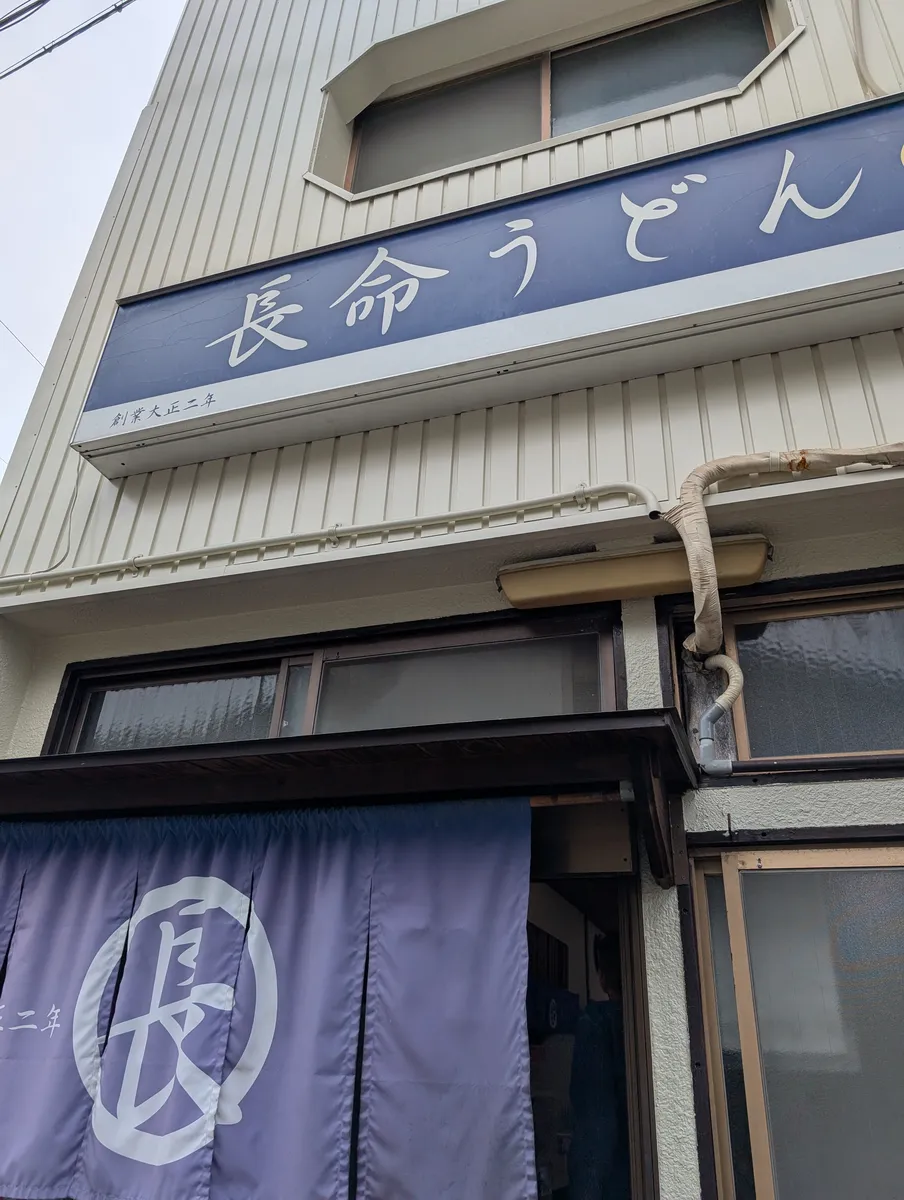 The blue signboard and indigo noren curtain of a noodle shop on a Nagoya street.