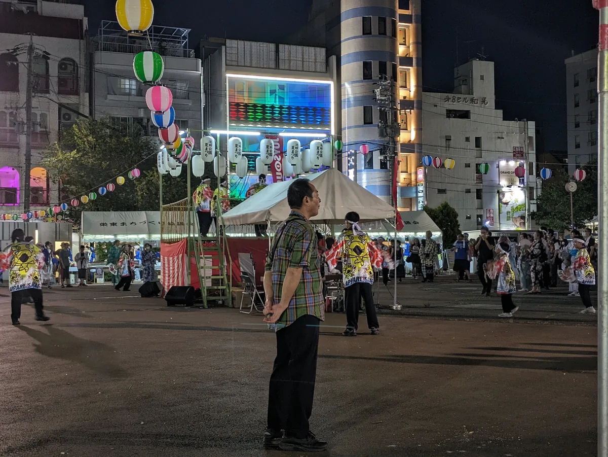 White tents and strings of round paper lanterns at a night-time summer festival in a city square in Nagoya