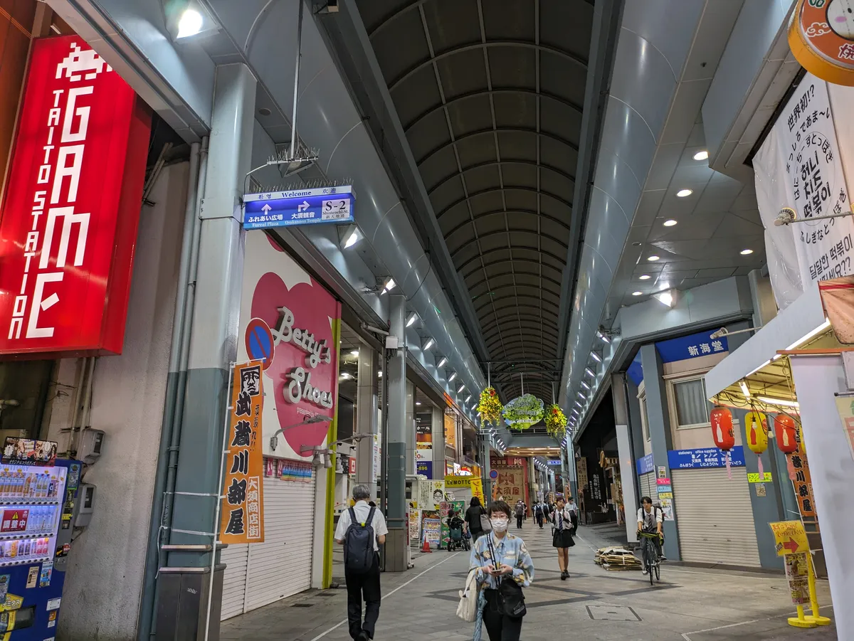 Shoppers walking through the covered Osu shopping arcade in Nagoya, past shopfronts, hanging lanterns and a bilingual direction sign.