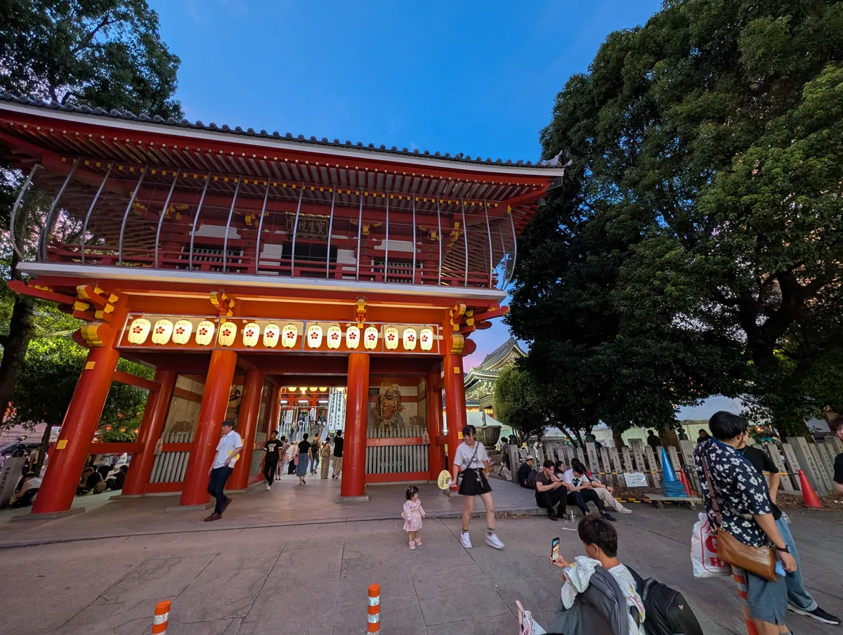 The red Nio gate of Osu Kannon hung with paper lanterns, with people crossing the paved forecourt beneath it