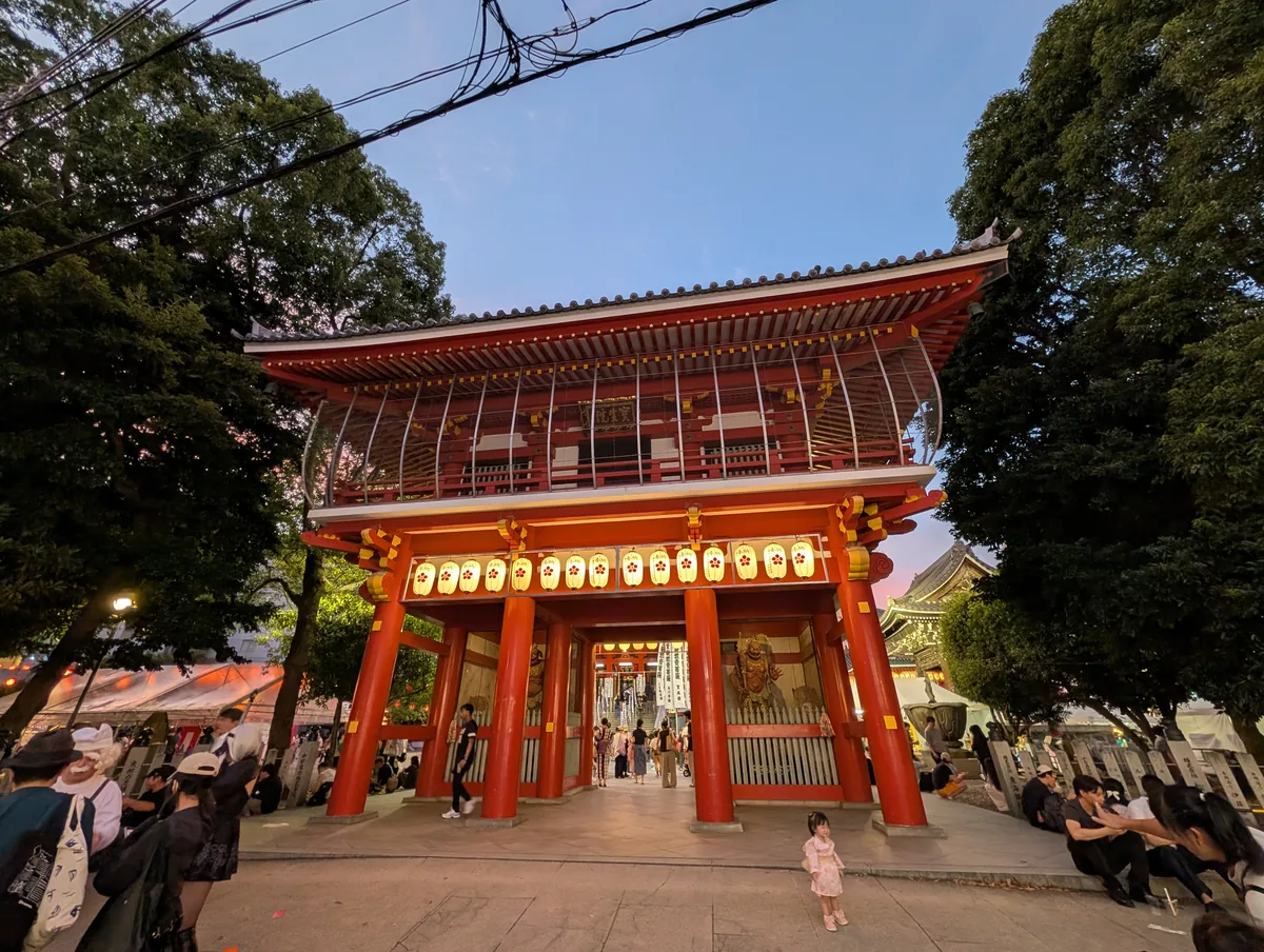 The red gate of Osu Kannon lit with paper lanterns at dusk, with white festival stall tents along the grounds