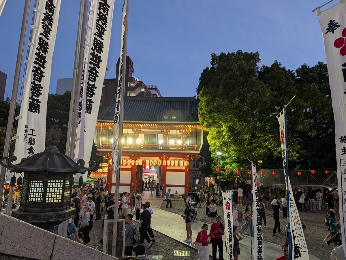 Osu Kannon temple hall lit up at dusk with red lanterns strung across the grounds and visitors walking below