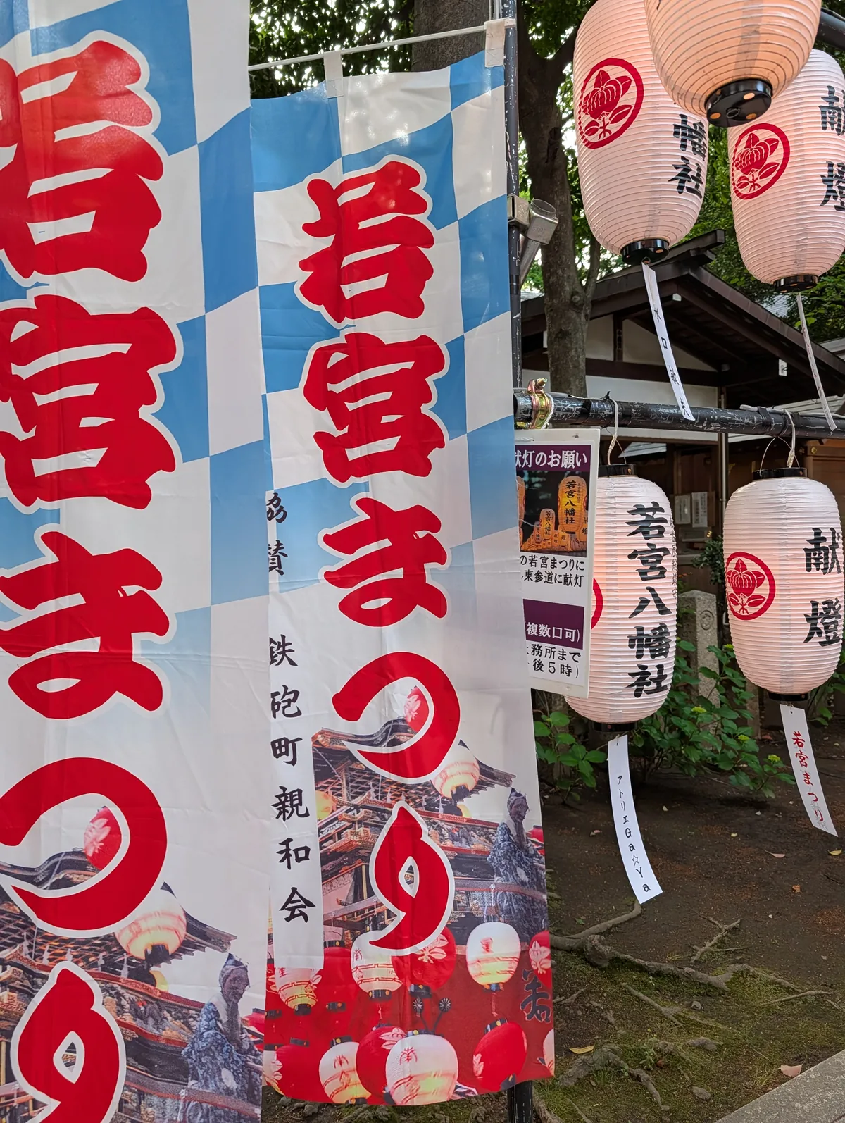 A blue and white banner reading Wakamiya Matsuri in red brush characters, beside paper lanterns at a Nagoya shrine