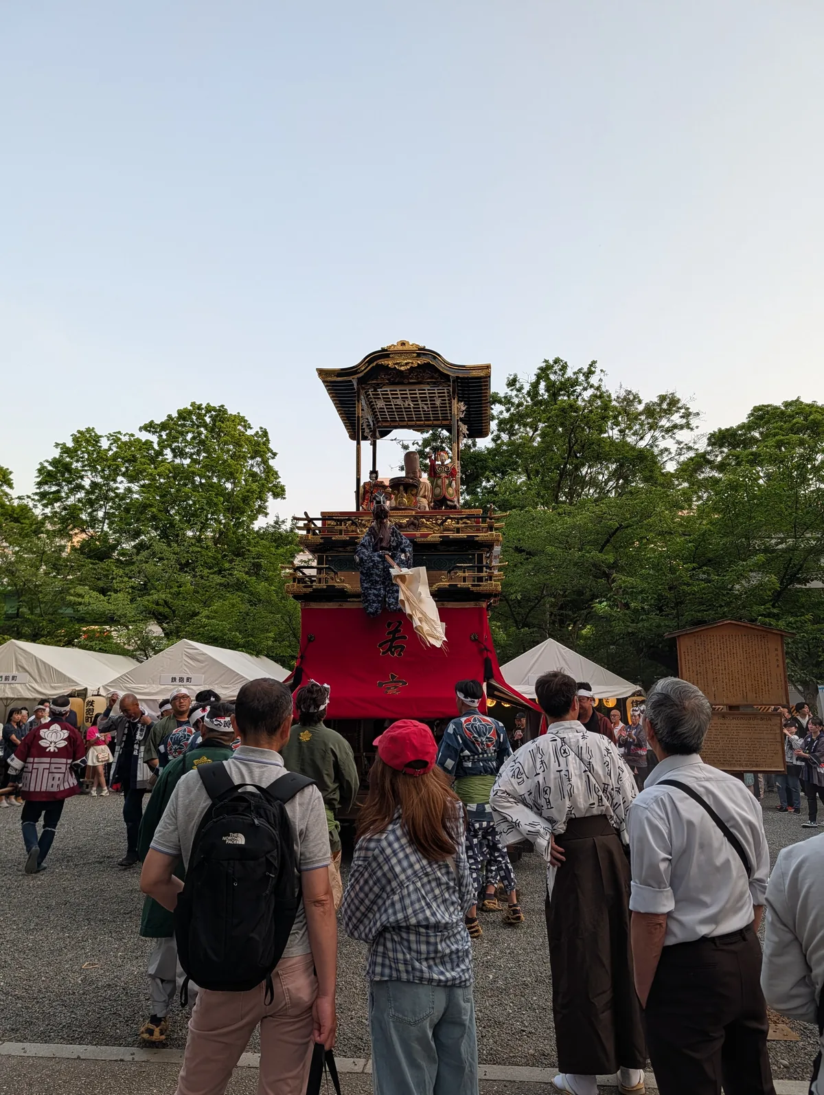 A festival float with karakuri puppets on its upper deck, surrounded by participants in happi coats and onlookers
